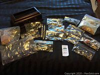 Multiple costume jewelry pieces in plastic bags and two wristwatches on black cloth with wood box
