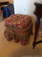 Side view of the skirted upholstered stool showing floral patterned cushion, skirted fabric base, and tassel fringe details.
