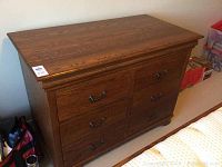 Solid wood dresser with six drawers and metal handles, finished in warm brown wood tone.