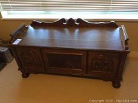 Overall front view of cedar chest under window, showing carved panels, top surface and back gallery rail.