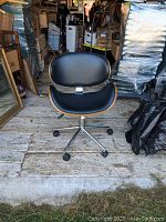 Front view of the modernist office chair showing black cushioned seat and backrest with bent plywood sides and metal swivel base with wheels.