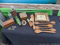 Photo showing seven wooden spoons and utensils, a whisk brush, a pottery green alligator bank, glass bottles, candle holders, and a small wooden box.