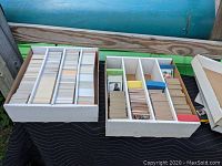 Two white boxes filled with numerous sports cards organized in compartments, mostly football cards from early 1980s.