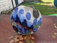 Front view of vase on tripod legs with scalloped rim and multicolor glaze