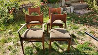 Four mid-century modern dining chairs arranged outdoors on grass, one with armrests, all with brown upholstered seats and bowtie backrests.