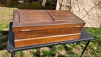 Rectangular wooden tool chest on a black table outdoors, showing the raised panel top and overall condition.