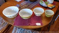 Four nested Pyrex bowls displayed on a round wooden table with one price tag visible on the smallest bowl.