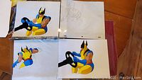 Photo showing three animation cells of Wolverine in yellow and blue costume holding a black steering wheel or similar object from various angles, and one blank visible sheet with pencil sketch.