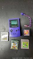 Purple Nintendo Game Boy Color with 5 game cartridges and purple flexible LED lamp accessory arranged on black surface.