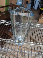 Clear triangular glass vase standing upright on metal rack, showing front and side profile.
