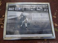 Framed black and white photo showing pitching moment during Don Larsen's perfect game with printed box score and lineup, including visible signature.