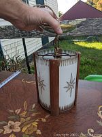 Front angle of mid-century pendant showing wood strips and curved glass panel with gold starburst design.