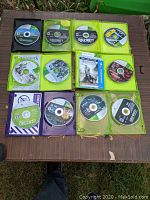 Top view of 14 Xbox 360 game discs laid out on a wooden surface showing most titles and cases.