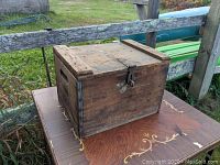 Front and side view of the antique wooden milk box placed on a decorated wooden table outside.