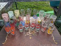 Full overview shot of all glasses showing variety in colors, sizes, and decorations including floral, bee, and character motifs.