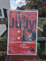 Full image of the vintage movie poster titled It's Judy featuring Judy Garland with a microphone and bright red background.