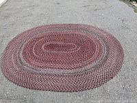 Full view of the oval braided rug laid flat on a rough tool surface, showing its full size and shape
