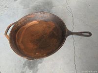 Top-down photo of a large Lodge #10 cast iron skillet showing surface rust and wear on the cooking surface, placed on a concrete floor.