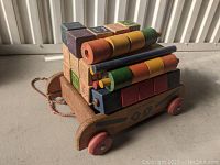 Side view of wooden pull wagon loaded with stacked wooden alphabet blocks and cylinder pieces.