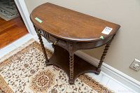 Front angle view of antique demi lune table showcasing carved spiral legs, drawer front, and shape of table top.