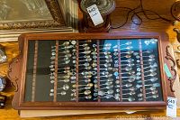 Top view of one wooden wall-mounted display cabinet with collectible souvenir spoons inside.