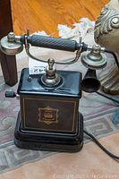 Front view of telephone showing metal body with crest, handset cradle and crank handle