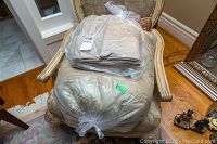 King size bedding set including a comforter and sheets on a patterned armchair, both sealed in plastic bags.