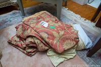 Folded bedding and curtains with floral tapestry pattern piled on carpet floor