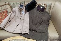 Two women's jackets and one black rabbit fur hat laid on sofa
