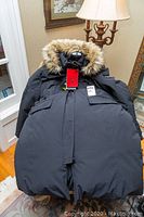 Full view of black men's winter coat with fur-trimmed hood laid on a chair.