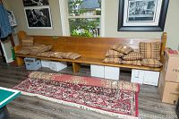 Full view of the antique wooden church pew bench with cushions on it and some boxes underneath the bench, showing overall condition and environment.