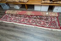 Partial roll showing one corner of the rug, emphasizing the floral geometric woven pattern and beige fringes