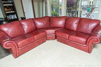 Full view of the red leather sectional sofa showing all three pieces arranged in an L shape in front of large windows.