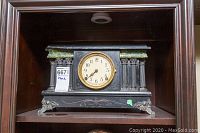 Full frontal shot of the antique black mantel clock featuring decorative columns and metal feet.