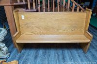 Front and side view of an antique wooden church pew bench showcasing the high backrest, flat seat, and armrests with visible wood grain and some signs of aging.