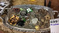 Top view of an ornate silver-toned tray holding an assortment of vintage brooches in various styles such as flowers, butterflies, and clusters.