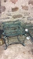 Two end tables with wrought iron scrollwork bases and square glass tops against a stone wall.
