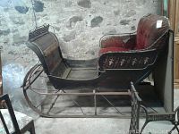 Full side view of wooden sleigh showing runners, body and upholstered seat