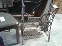 Side view of Singer treadle sewing machine base showing brand name and pedal area.