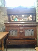 Front view of wooden cabinet showing the upper drawers, glass paneled doors, and bottom drawer with carved details.