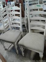 Four white wooden ladder back chairs with upholstered seats arranged closely together showing general condition and style.