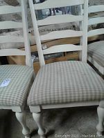 Photo shows close-up of chair seats and legs highlighting beige and white checkered upholstery and cream painted wooden frame.