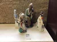 Front view of all four ceramic statues grouped together on a shelf with a label in front