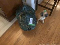 Cast iron coal scuttle next to resin pug dog statue on wooden floor, clearly showing ornate cast iron design and green enamel lid.