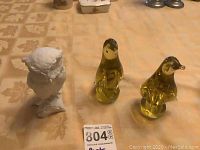 Photo showing three figurines: white porcelain owl on the left with two yellow glass birds on the right, along with the lot number card.