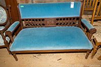 Full front view of antique settee highlighting blue velvet seat and carved wooden backrest and arms