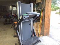 Folded black treadmill stored inside barn, showing overall shape and fold-up design.