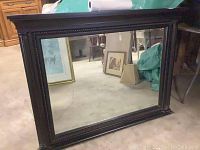 Front view of large rectangular mirror with dark wood frame and carved details around the edges.