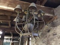 Rustic metal chandelier with 9 arms and small metal shades, hanging in a barn setting showing rustic stone walls and ceiling beams.