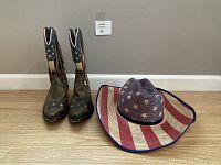 Photo showing the Dan Post cowboy boots and Bullhide American flag print cowboy hat side by side on wooden floor against gray wall.